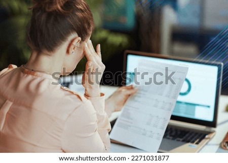 Seen from behind modern female with documents and laptop having headache in modern office. Royalty-Free Stock Photo #2271031877