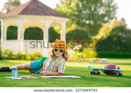 Summer leisure with children. Child drawing picture with crayon in summer park outdoor. Happy little kid boy holding a brush to paint with toys for playing outdoor.