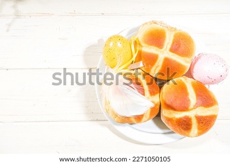 Traditional spring holiday Easter baking pastry – hot cross buns. On light wooden background with sunlight, Easter eggs, decor and spring branches
