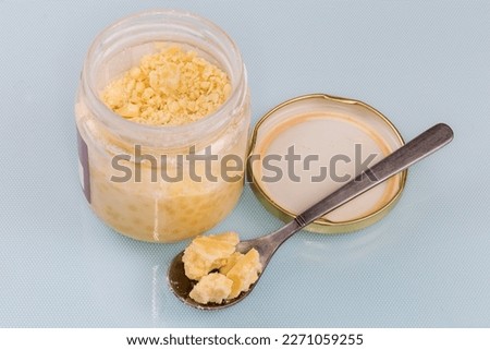 Raw partially crumbled solid cocoa butter in the small glass jar with removed lid and pieces in a tea spoon on a blue surface
 Royalty-Free Stock Photo #2271059255