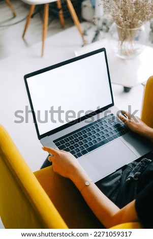 Young caucasian woman sitting on sofa at home and using laptop computer with white blank screen, mock-up.