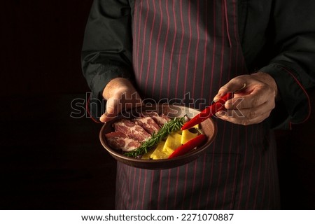 The cook puts red peppers on a plate with sliced ham and cheese. Dark space for recipe or menu.