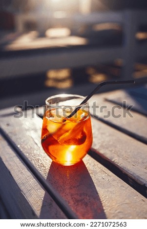 Orange slice and aperol spritz cocktail on a stone against the backdrop of a sandy beach. Glass with iced citrus sparkling mineral water and straw. Long shadows. Top view. Copy space. Royalty-Free Stock Photo #2271072563