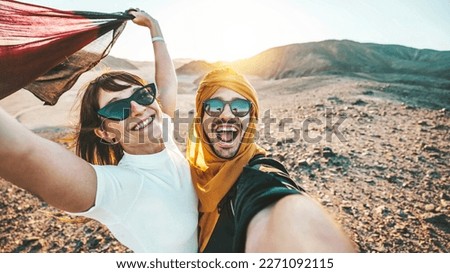 Happy couple of travelers taking selfie picture in rocky desert - Young man and woman having fun on summer vacation - Two friends enjoying summertime moment - Life style and travel concept
