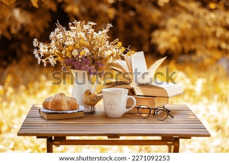 Bouquet of flowers, croissant, cup of tea or coffee, books on table in autumn garden. Rest in garden, reading books, breakfast, vacations in nature concept. Autumn time in garden on backyard Royalty-Free Stock Photo #2271092253