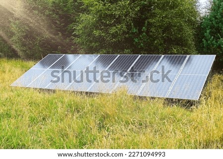 Ground array of  Solar panels placed in front of bushes and surrounded by long grass   Royalty-Free Stock Photo #2271094993