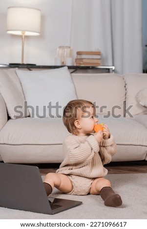 Side view of baby girl holding toy near laptop at home in living room