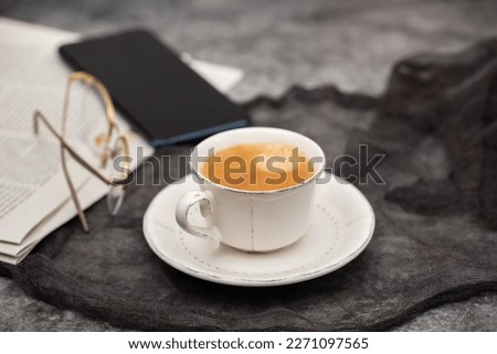 Newspapers and white coffee cup, with reading glasses.