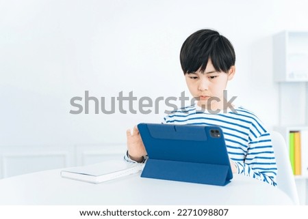 Asian little boy studying while looking at a tablet. Online class. e-learning. Ed tech.