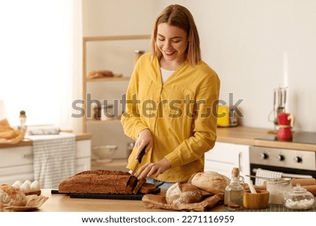 Young woman cutting rye bread at table in kitchen Royalty-Free Stock Photo #2271116959