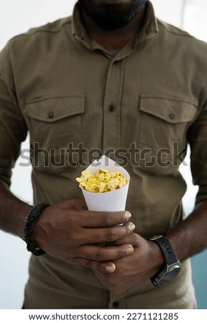 A person holding a paper cone with popcorn, Popcorn lover's day concept Selective focus