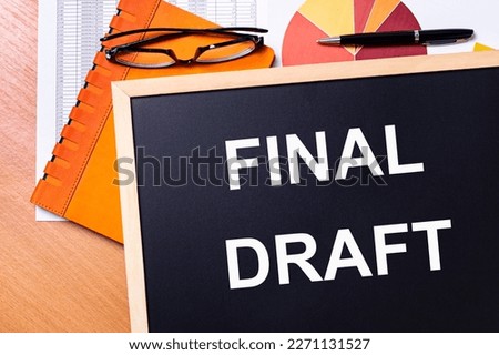 On the office table is an orange notepad, black glasses, a pen and a note-board with the text FINAL DRAFT