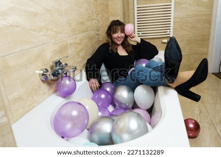 Young Woman Sitting in a Bathtub Full of Balloons in Bathroom