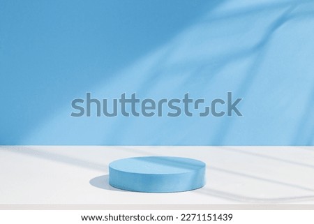 Pastel blue cylinder shape podium on white table against bright wall background with window shadows. 