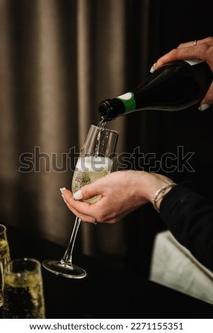Woman pours champagne into a flute glass. Champaign is being pored into glasses. Waiter pouring white sparkling wine. Bottle in a closeup view. Catering service concept. Royalty-Free Stock Photo #2271155351