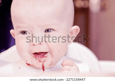 Happy childhood and delicious food. Funny child gets dirty with food. Little cute kid eats with his hands. Grimaces of a cheery baby. Close-up of a child's face.