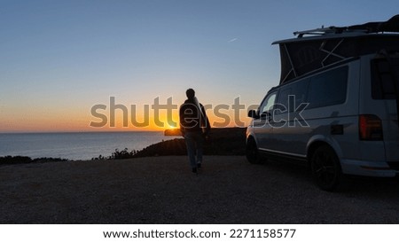 Surferboy sitting near his mini van and looking on the ocean at summer sunset  with a surfboard on her side Royalty-Free Stock Photo #2271158577