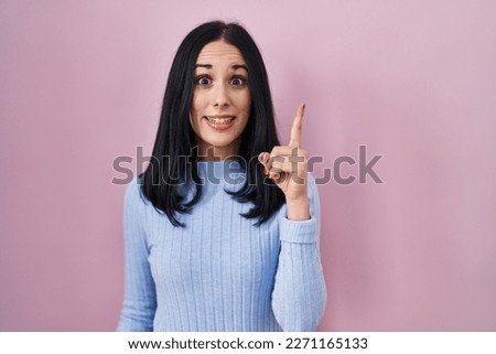Hispanic woman standing over pink background pointing finger up with successful idea. exited and happy. number one. 