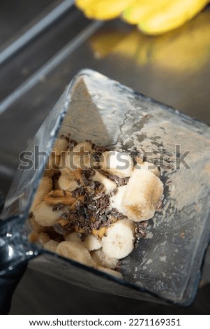 A view looking into a blender pitcher, featuring frozen banana, cacao nibs and peanut butter.