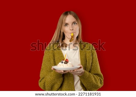 Holidays and celebration. Excited woman celebrating birthday, blowing candle on cake, wearing party cake and having fun, standing over red background. 