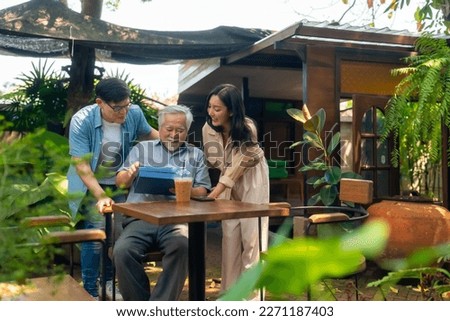 Asian couple surprised elderly father with gift box at outdoor cafe restaurant on summer holiday vacation. Family relationship, celebrating birthday, father's day and older people health care concept.