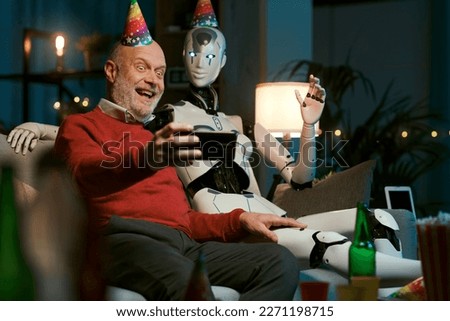 Lonely senior man having a party at home with his humanoid AI robot, they are taking selfies with a smartphone
