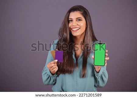 Horizontal photo. Beautiful Brazilian woman, with casual clothes, Jeans and green shirt. smartphone with green screen and cards.