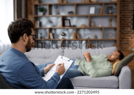 A visit to the psychologist of an African American man. A handsome man is lying on the couch and talking to a psychotherapist. Depression, apathy, stress, burnout at work. Help of a psychologist. Royalty-Free Stock Photo #2271202495