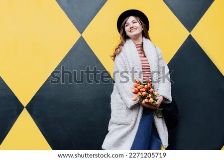 Happy. emotional young fashion woman holding bouquet of fresh tulip flowers on the geometry bright yellow and black wall background. Urban city street fashion. Spring mood, women day. Selective focus.