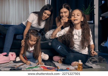  Staged photo. A lesbian couple and their children are having a good time at home.    The girls are playing on the floor. The older girl blows a lot of soap bubbles.                              