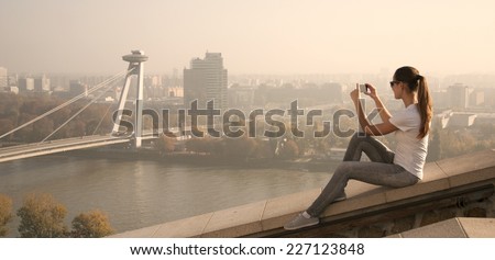 girl sitting over the city over the river and take pictures
