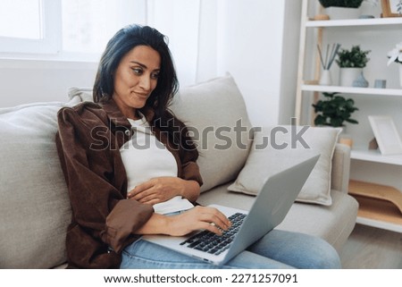 Woman freelancer on her day off sitting on the couch with a laptop at home and watching series and tv shows, smile
