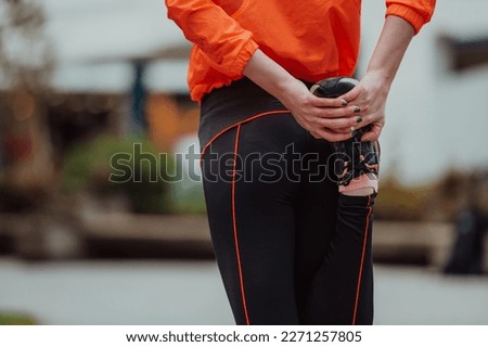 Fit attractive woman in sportswear stretching one leg before jogging on the footpath outdoor in summer among greenery. Workout, sport, activity, fitness, vacation and training concept.