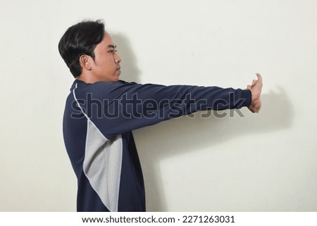 asian man gesture stretching hands or warming up. indonesian man smiling and looking at camera wearing navy sweater or sportswear on isolated white background. portrait of people exercising
