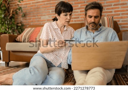 Happy senior husband, wife, mature couple, family, Caucasian mature, adult and retiree using laptop with credit card, shopping online at home, paying for groceries, paying by browsing internet.