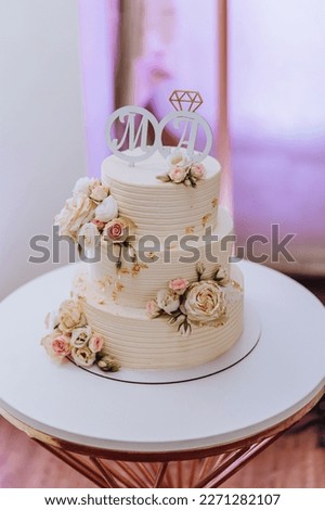 White wedding cake with flowers and blueberries. A beautiful home wedding three-tiered cake decorated with pink roses in a rustic style on wooden table