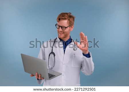 a young doctor with a laptop in his hands consults a patient via video conference on a blue background in the studio