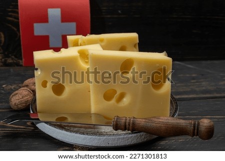 Block of Swiss medium-hard yellow cheese emmental or emmentaler with round holes and cheese knife and flag of Switzerland close up Royalty-Free Stock Photo #2271301813