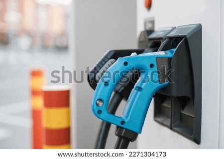 Electric charging station with blue and black power cords. Blurred background of urban area. Eco friendly transport and zero emission concept.