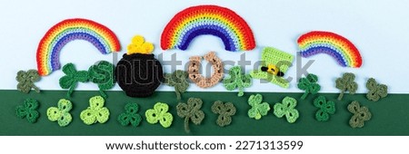 St Patrick's Day concept. Knitted composition of a green hat, a pot of gold, a horseshoe, a rainbow and green shamrocks on a green and blue background. Banner