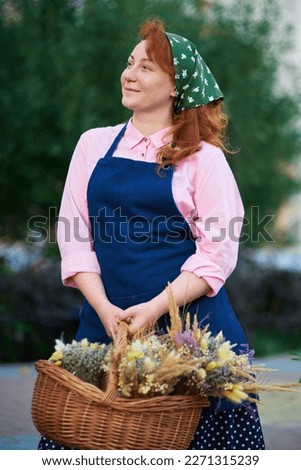 farm woman in apron with basket of dried flowers outdoor, village life. Florist woman with lavender bunches . High quality photo