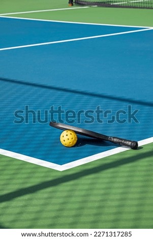 View of a pickleball complex with a paddle and yellow ball on blue and green courts beside a playground in a suburban park in early spring. Royalty-Free Stock Photo #2271317285