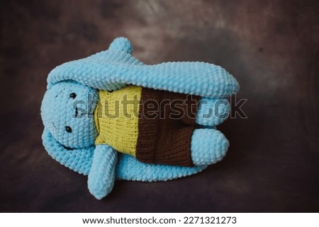 a blue knitted rabbit with big ears in a yellow vest and brown pants in a photo studio on a beautiful background
