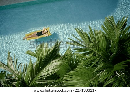 Enjoying suntan. Tropical vacation concept. Top view of young woman on the yellow air mattress in the swimming pool with palm trees. Royalty-Free Stock Photo #2271333217