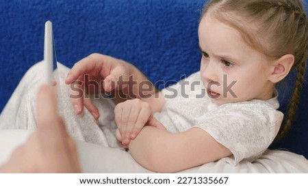 Kid, daughter resting using digital tablet while lying on sofa with dad. Child holding tablet in his hands, watching childrens cartoon on Internet, playing games at home. Childrens entertainment