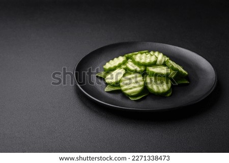 Delicious healthy raw cucumber sliced on a black ceramic plate on a dark concrete background