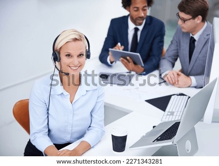 Let me make your day. Portrait of businesswoman wearing a headset with her colleagues sitting in the background.