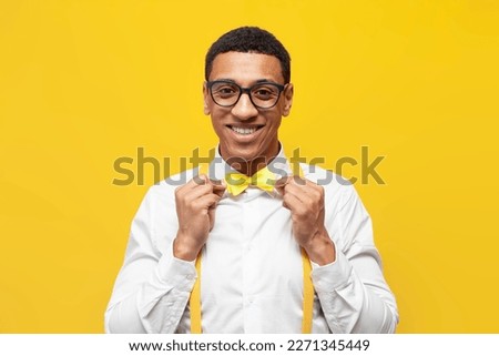 young african american guy in festive outfit with bow tie and suspenders on yellow isolated background, nerdy man in glasses smiles and poses