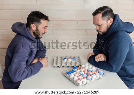 Bearded men play chess with Easter eggs at white table. Creative ideas for unusual chess. Colorful painted egg figures. High quality photo