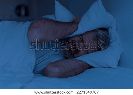Closeup of angry mature man lying in bed and covering head ears with pillow at night, cannot sleep, suffering from noisy neighbours or snoring spouse partner Royalty-Free Stock Photo #2271349707